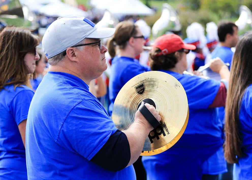 Alumni band member playing cymbals with other band members in the background