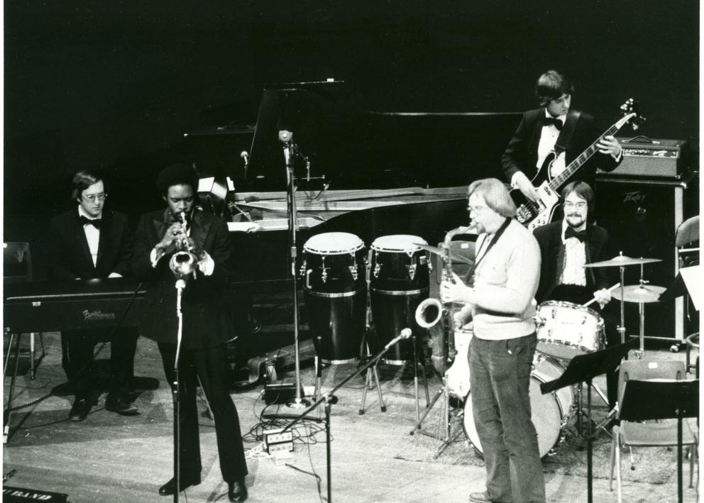 a black and white photo of jazz musicians onstage in front of microphones