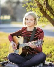 Music Therapy student playing guitar on grass in the sunshine