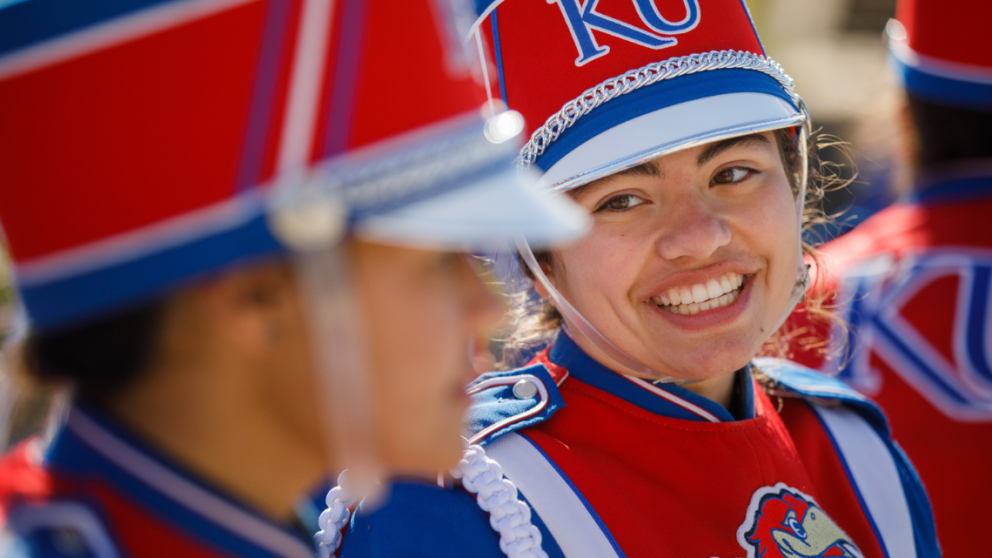 a woman dressed in a marching jayhawks uniform smiles